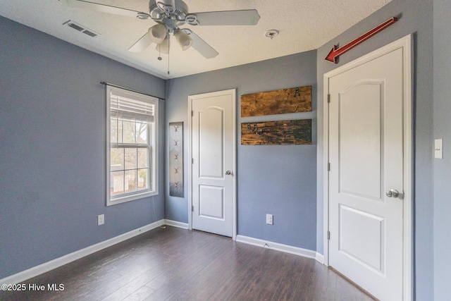 unfurnished bedroom featuring visible vents, baseboards, a ceiling fan, and dark wood-style flooring