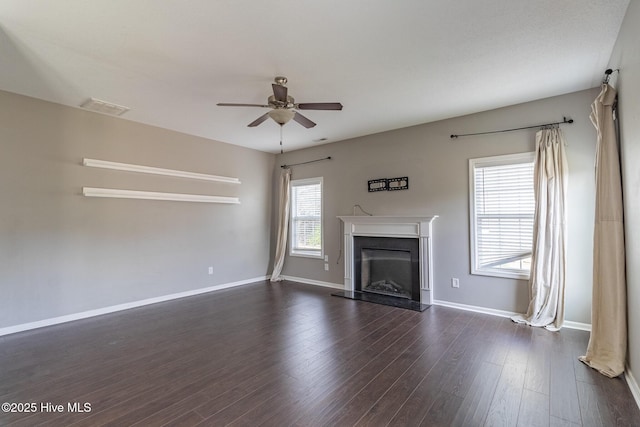 unfurnished living room with visible vents, a fireplace with raised hearth, a ceiling fan, dark wood-style floors, and baseboards