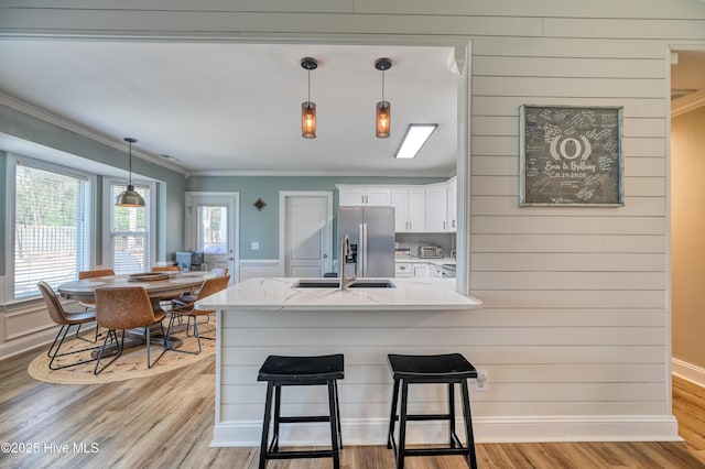 kitchen featuring light stone counters, a breakfast bar, ornamental molding, white cabinets, and stainless steel refrigerator with ice dispenser