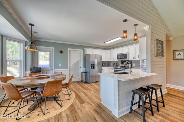 kitchen featuring appliances with stainless steel finishes, a peninsula, light wood-style floors, white cabinetry, and a sink