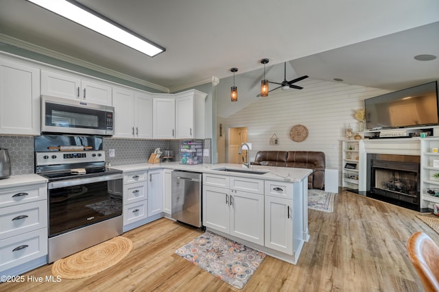 kitchen featuring a sink, open floor plan, a peninsula, appliances with stainless steel finishes, and a fireplace