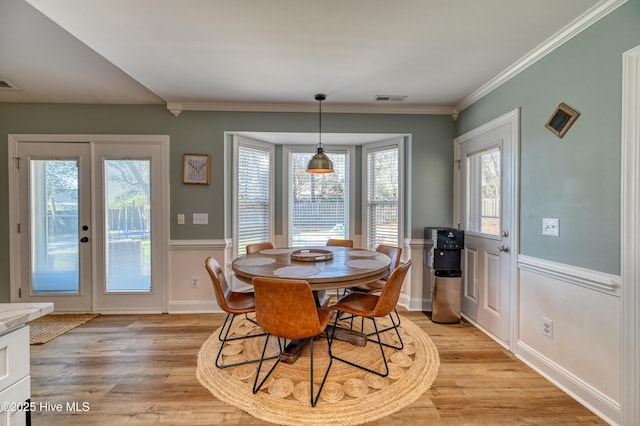 dining room with crown molding, light wood-style floors, visible vents, and french doors