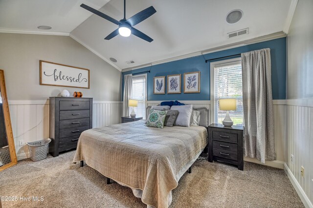 carpeted bedroom featuring a wainscoted wall, lofted ceiling, visible vents, and ornamental molding