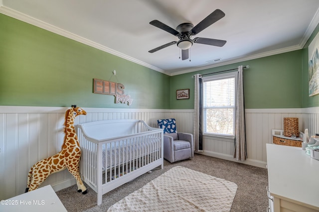 bedroom featuring visible vents, carpet flooring, a nursery area, and a wainscoted wall