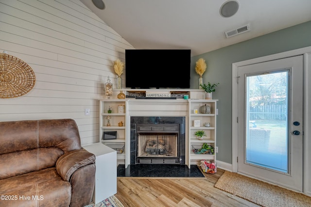 living room featuring a high end fireplace, visible vents, baseboards, lofted ceiling, and wood finished floors