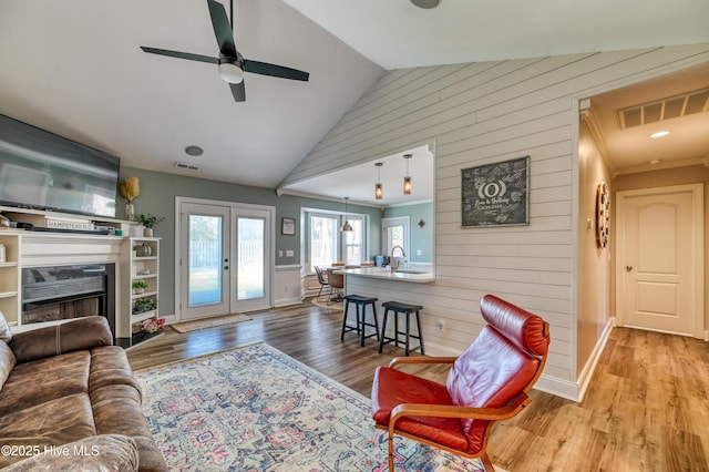 living area with visible vents, wood finished floors, french doors, a fireplace, and vaulted ceiling