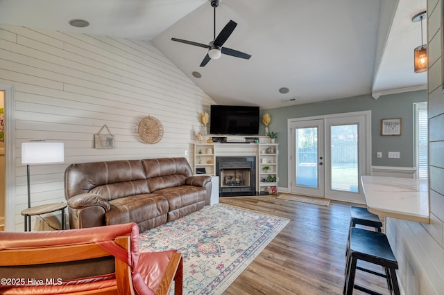 living area featuring wood finished floors, visible vents, a ceiling fan, a fireplace, and vaulted ceiling