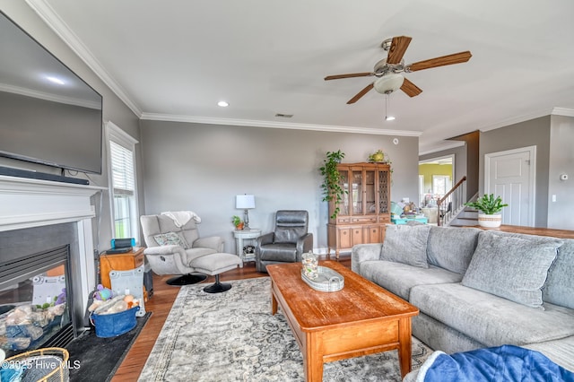 living room featuring visible vents, ceiling fan, stairs, wood finished floors, and a glass covered fireplace