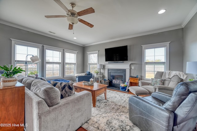 living area with visible vents, a fireplace with flush hearth, a healthy amount of sunlight, and ornamental molding