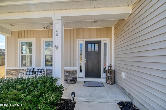 view of exterior entry featuring stone siding and covered porch