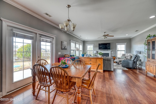 dining space with visible vents, ornamental molding, a fireplace, and wood finished floors