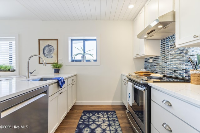 kitchen with dark wood-style flooring, stainless steel appliances, white cabinets, under cabinet range hood, and tasteful backsplash