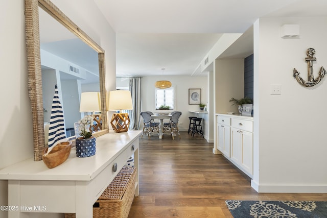 hallway with dark wood-type flooring, baseboards, and visible vents