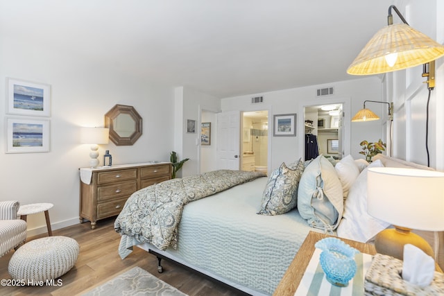 bedroom with a spacious closet, visible vents, baseboards, wood finished floors, and ensuite bath