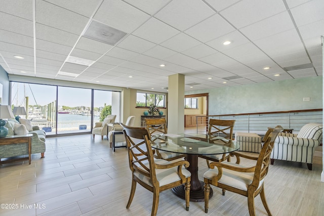 dining space featuring a drop ceiling, recessed lighting, a wall of windows, and a water view