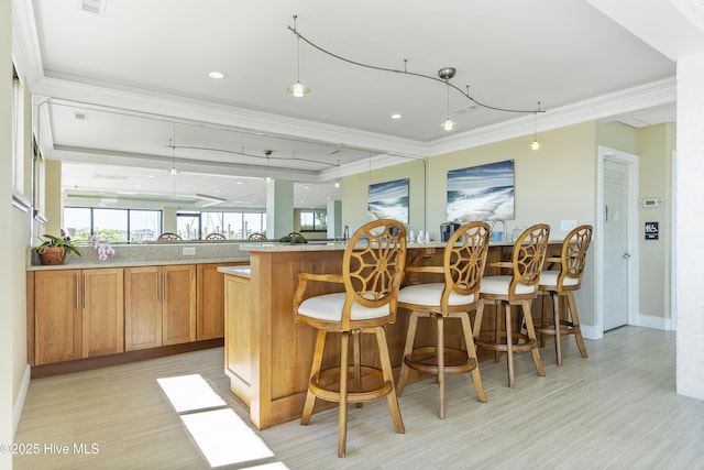 kitchen featuring crown molding, light stone countertops, decorative light fixtures, a breakfast bar area, and brown cabinetry