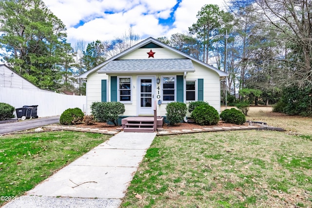 bungalow-style home with roof with shingles, a front yard, and fence