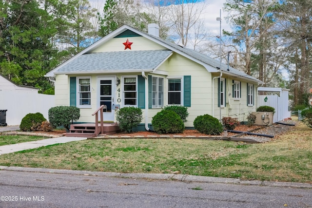 bungalow featuring a chimney, a shingled roof, a front lawn, and fence