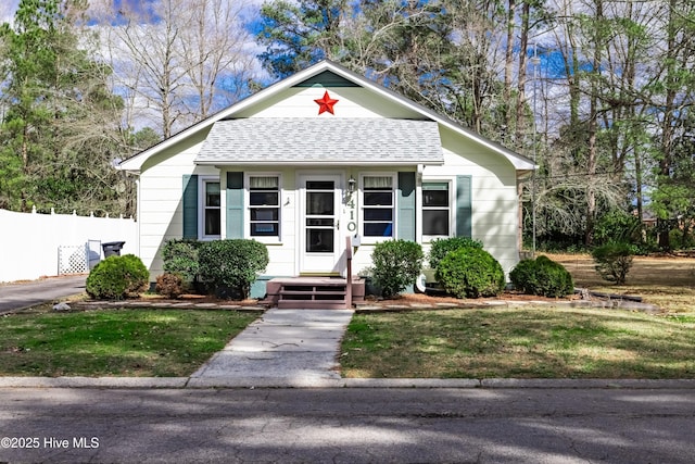 bungalow-style home featuring roof with shingles, a front lawn, and fence