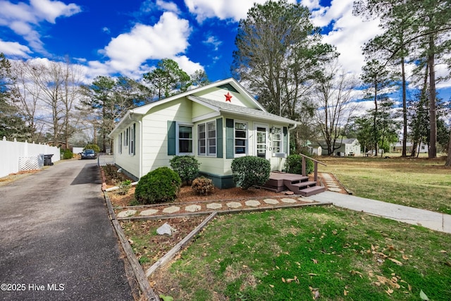 bungalow-style home featuring aphalt driveway, a front lawn, and fence