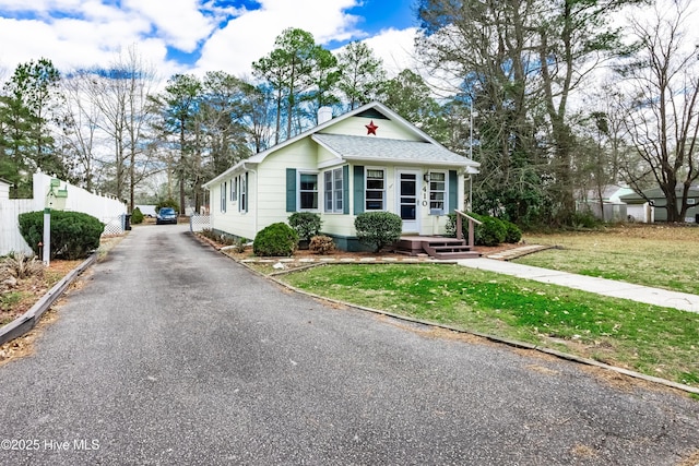 bungalow-style house with a front yard, fence, roof with shingles, driveway, and a chimney