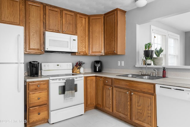 kitchen featuring white appliances, brown cabinetry, light countertops, and a sink