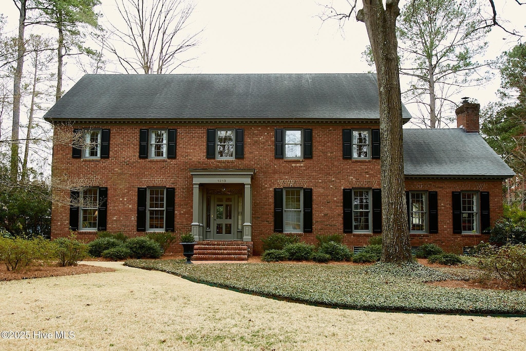 view of front of home featuring brick siding, a chimney, and a shingled roof
