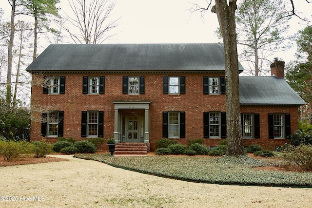 view of front of home featuring brick siding, a chimney, and a shingled roof