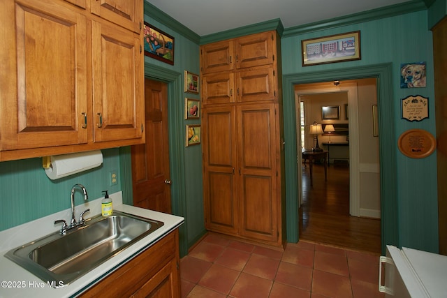 kitchen featuring light tile patterned floors, brown cabinetry, ornamental molding, a sink, and light countertops