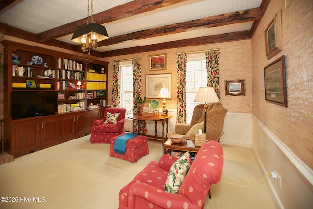 sitting room with beamed ceiling, plenty of natural light, carpet, and a wainscoted wall