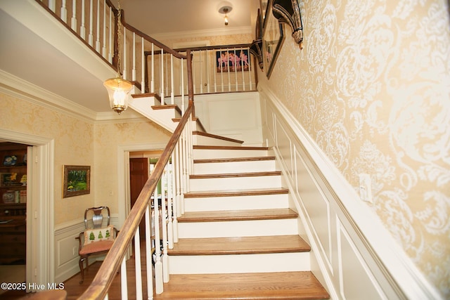 staircase with a wainscoted wall, wallpapered walls, a decorative wall, and ornamental molding