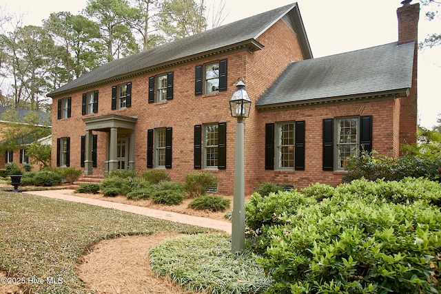 colonial-style house featuring brick siding and a chimney