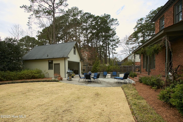 view of yard featuring an outbuilding, a detached garage, a patio, and fence