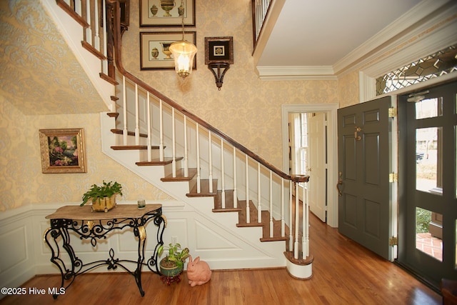 foyer entrance featuring wainscoting, wallpapered walls, ornamental molding, and wood finished floors