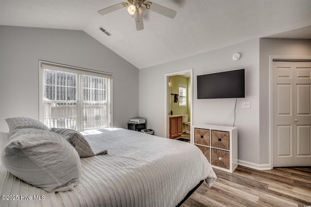 bedroom with wood finished floors, visible vents, baseboards, lofted ceiling, and ensuite bathroom