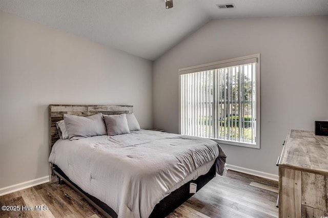 bedroom with visible vents, wood finished floors, baseboards, and vaulted ceiling