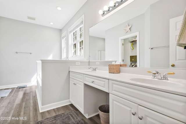 full bathroom featuring visible vents, a sink, wood finished floors, double vanity, and baseboards