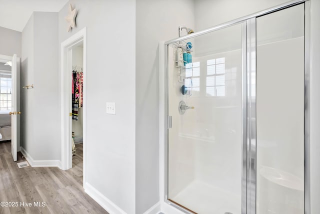 full bath with a stall shower, a walk in closet, baseboards, and wood finished floors