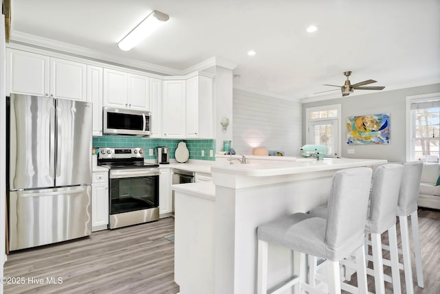 kitchen featuring tasteful backsplash, open floor plan, appliances with stainless steel finishes, a peninsula, and white cabinets