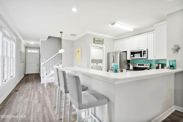 kitchen with washer and dryer, stainless steel appliances, backsplash, and ornamental molding