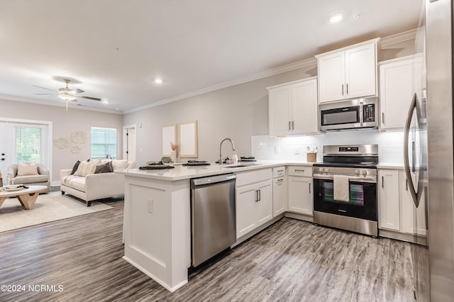 kitchen with tasteful backsplash, ornamental molding, a peninsula, white cabinets, and stainless steel appliances