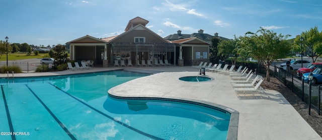 community pool featuring a hot tub, a patio, and fence