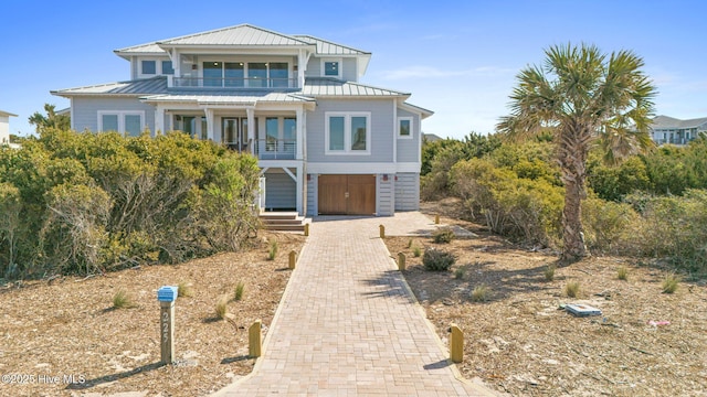 coastal home with a standing seam roof, metal roof, decorative driveway, and a balcony