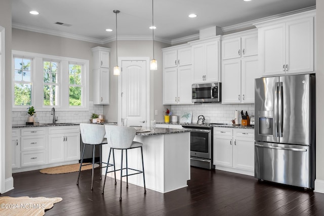 kitchen featuring visible vents, a kitchen island, dark wood-style floors, stainless steel appliances, and a sink