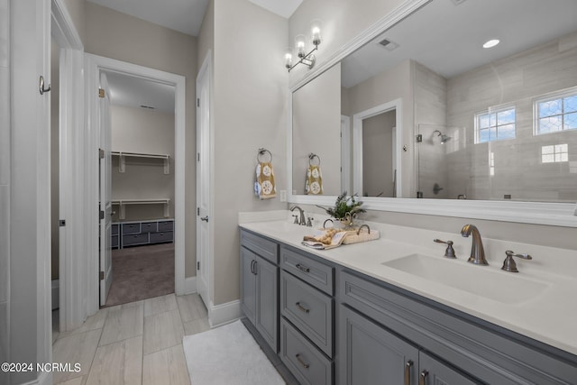 bathroom with double vanity, visible vents, a tile shower, and a sink