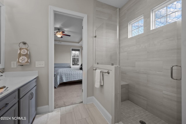 full bathroom with ceiling fan, baseboards, vanity, a tile shower, and ensuite bath