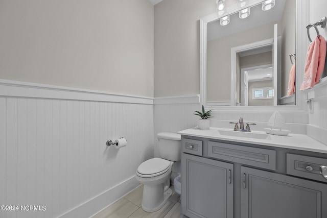 half bathroom with vanity, toilet, a wainscoted wall, and tile patterned flooring