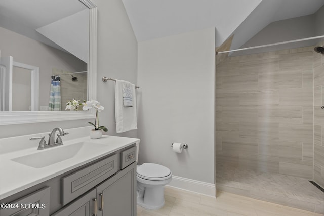 bathroom featuring vanity, baseboards, a tile shower, vaulted ceiling, and toilet