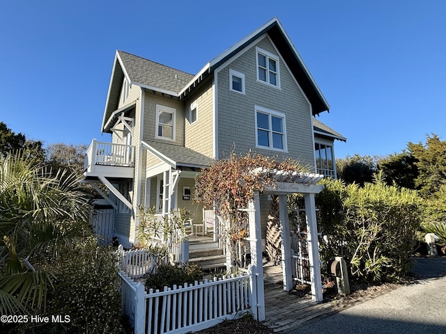 view of front facade with a balcony, covered porch, a fenced front yard, and roof with shingles