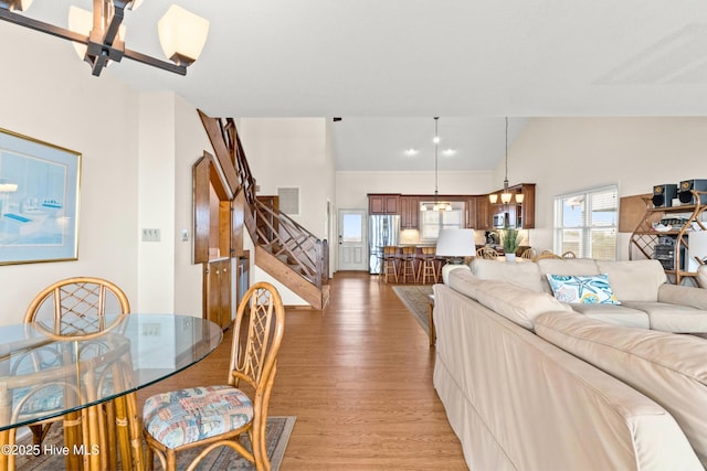 living room featuring visible vents, high vaulted ceiling, light wood-style flooring, stairs, and a chandelier